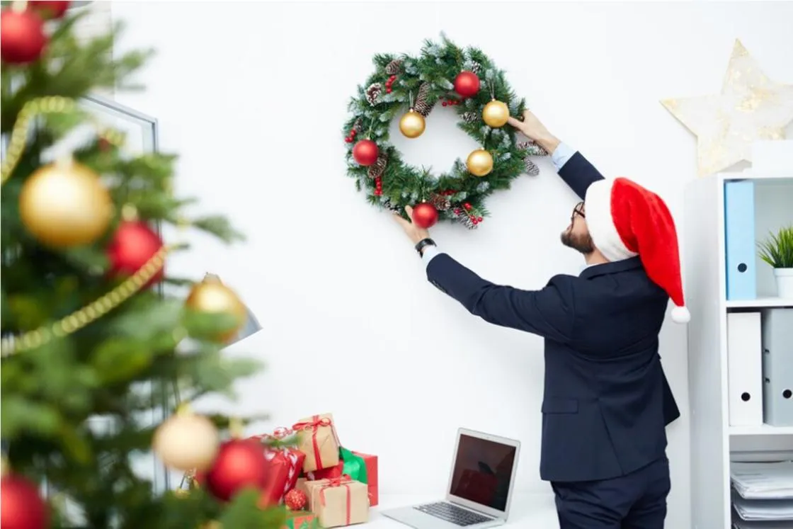 Офисный работник вешает на стену новогодний венок